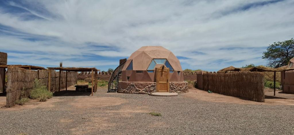 Real geodesic dome at Cabañas Laynaturi y Domo del Desierto, with a stone base, wooden door, and thatched reed fencing under an Atacama sky