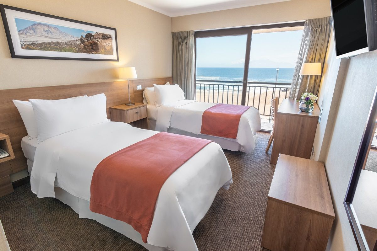 Geotel Antofagasta ocean-view room with two beds, wooden furnishings, and a balcony overlooking the Pacific